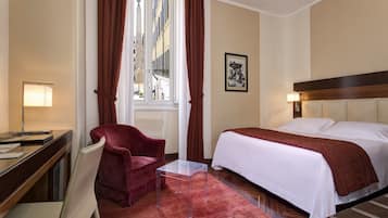 Habitación de hotel con cama, escritorio y silla, una mesita y ventana con cortinas.