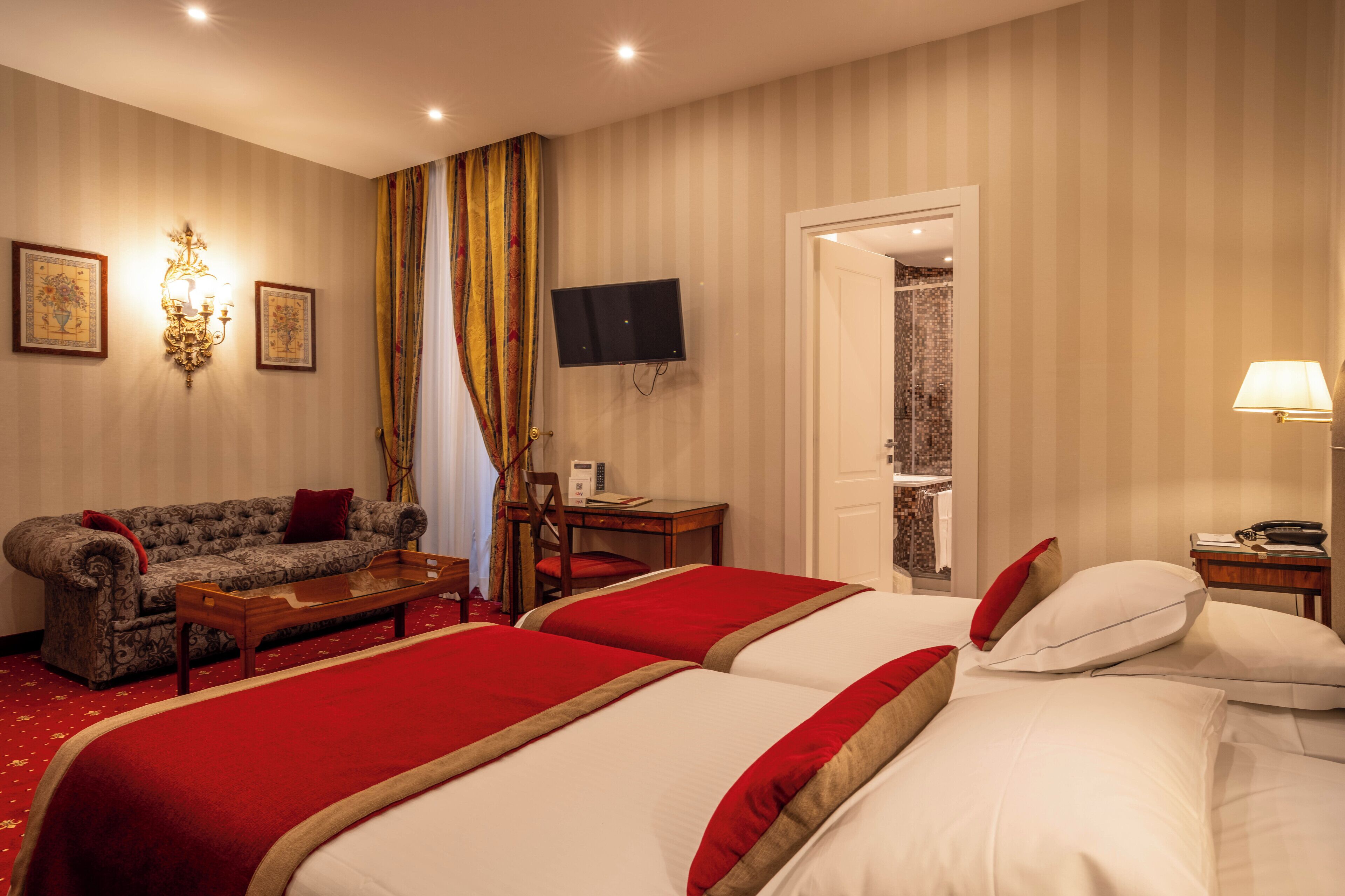 Camera d'albergo con due letti, un divano, una scrivania, una televisione e zona doccia.