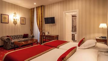 A hotel room with two beds, a sofa, a desk, a TV, and a shower area.