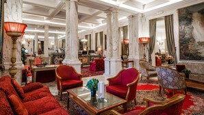 A luxurious lobby with marble columns, red upholstered furniture, and a large painting on the wall. - Hotel Nazionale (Rome)