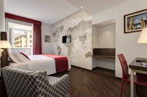 A hotel room with a bed, a desk, a chair, a TV, and a world map wall.