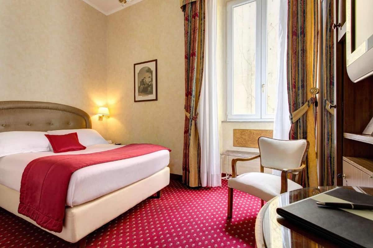 Ett hotellrum med en stor säng, ett skrivbord och en stol.