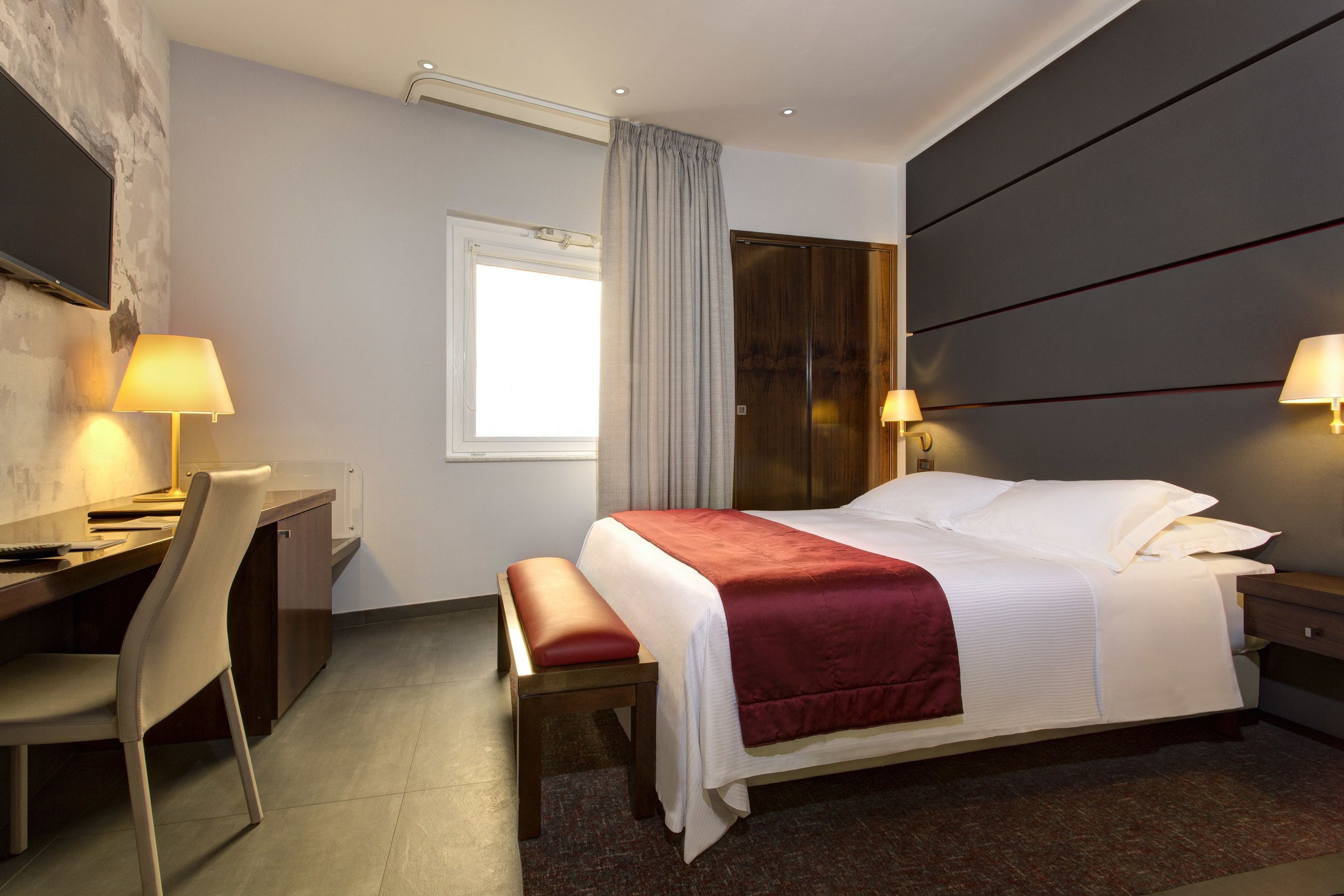 A hotel room with a bed, a desk, a chair, and a TV.