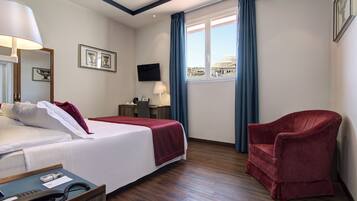 A hotel room with a bed, a desk, a chair, a TV, and a window with a view of a building.