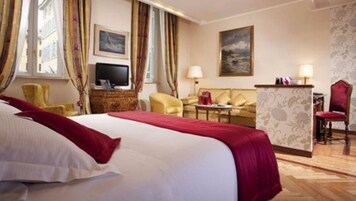 A hotel room with a large bed, a desk, a chair, a sofa, and two paintings on the walls.