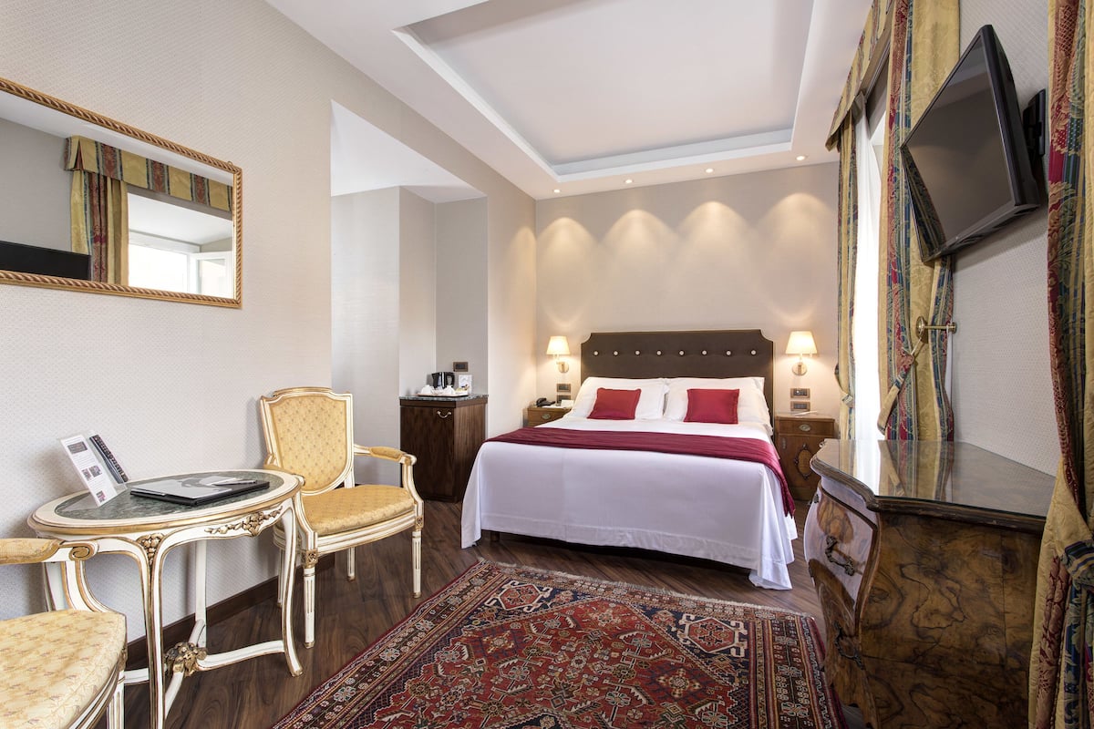 Ett hotellrum med en säng, sängbord, en stol, ett skrivbord, en tv och en stor spegel.