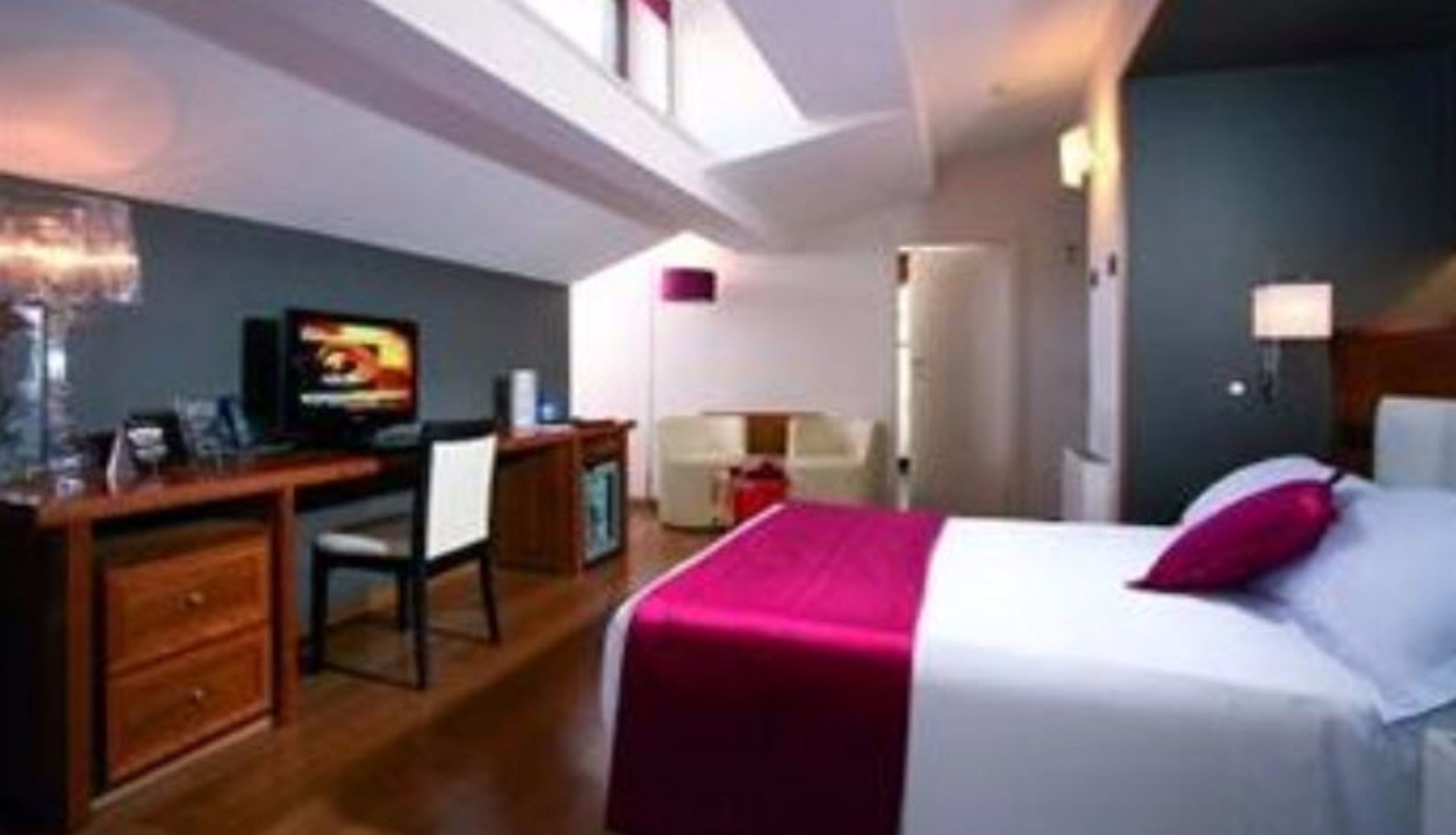 Quarto de hotel com cama, escrivaninha, cadeira e televisão.