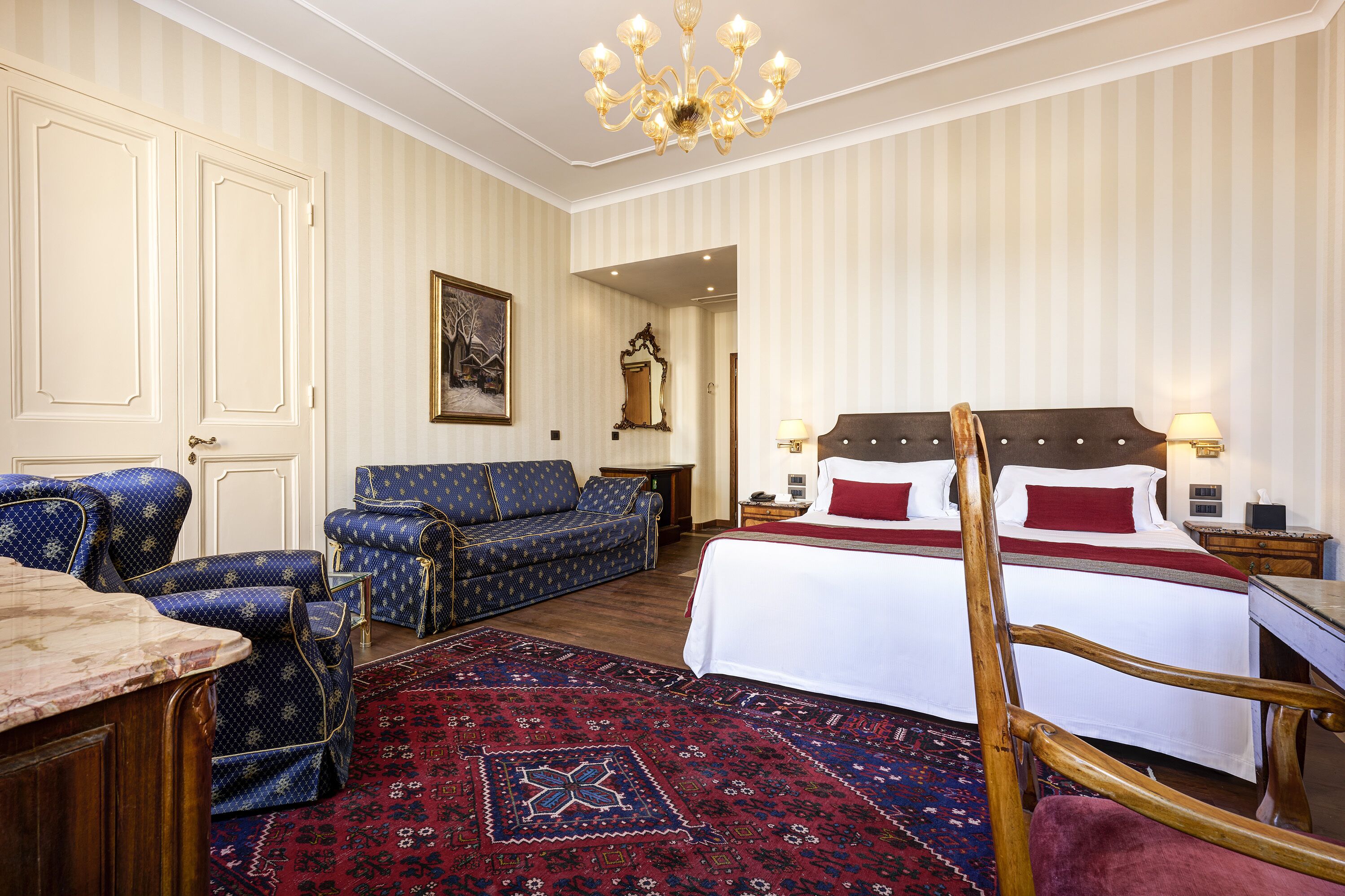 Ett hotellrum med en stor säng, en sittgrupp med en soffa, en trästol, ett skrivbord och en mönstrad matta.