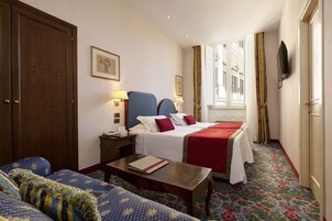 A hotel room with a large bed, a sofa, a wooden table, and a desk.