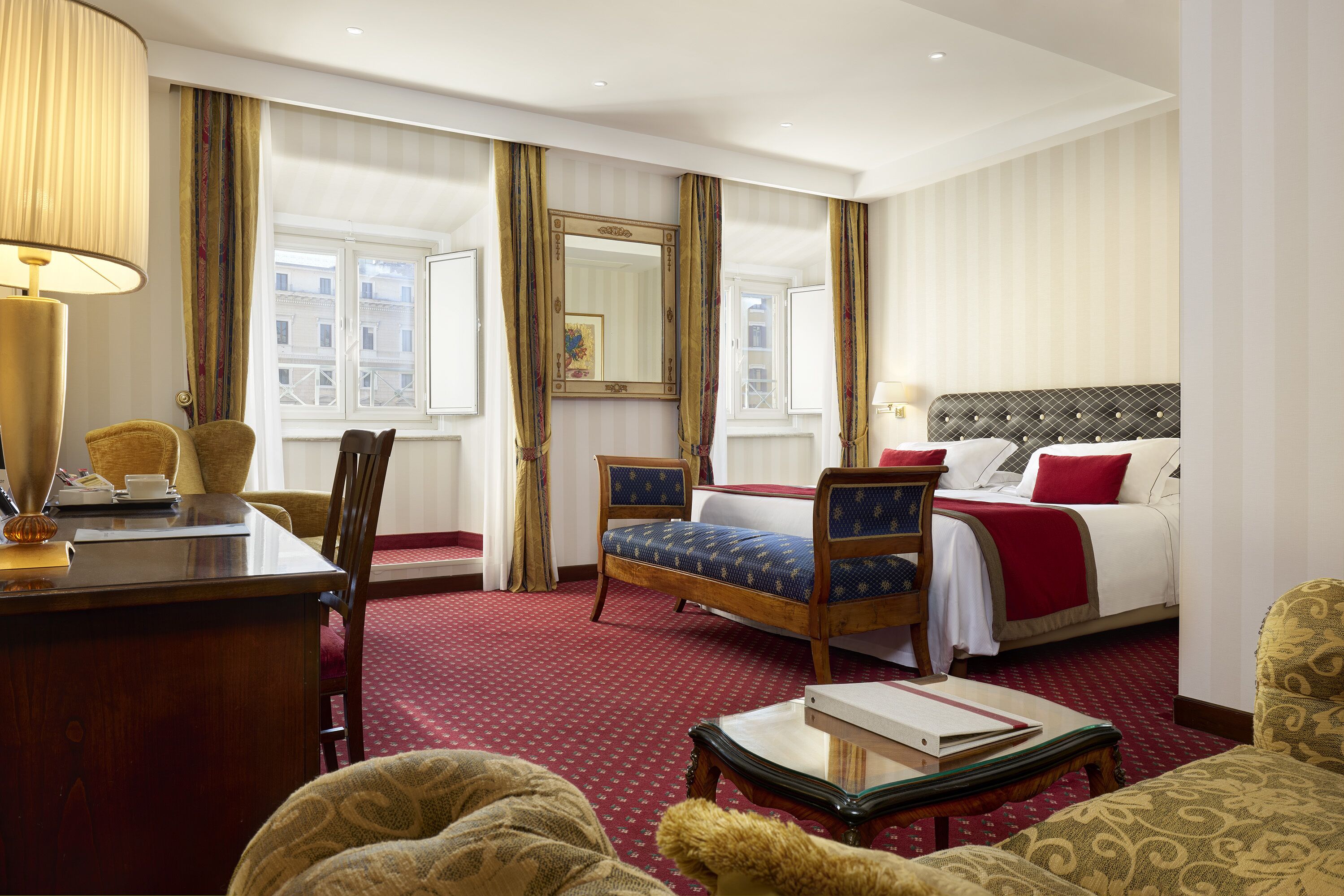 Une chambre d’hôtel avec un lit, un bureau, une chaise, une table et une grande fenêtre avec des rideaux.