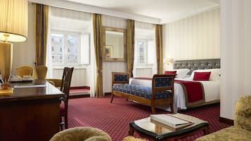 Quarto de hotel com cama, escrivaninha, cadeira, mesa e uma janela grande com cortinas.