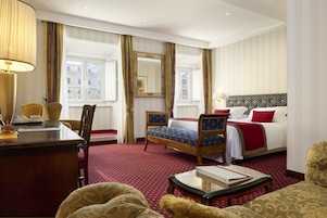 A hotel room with a bed, a desk, a chair, a table, and a large window with curtains.