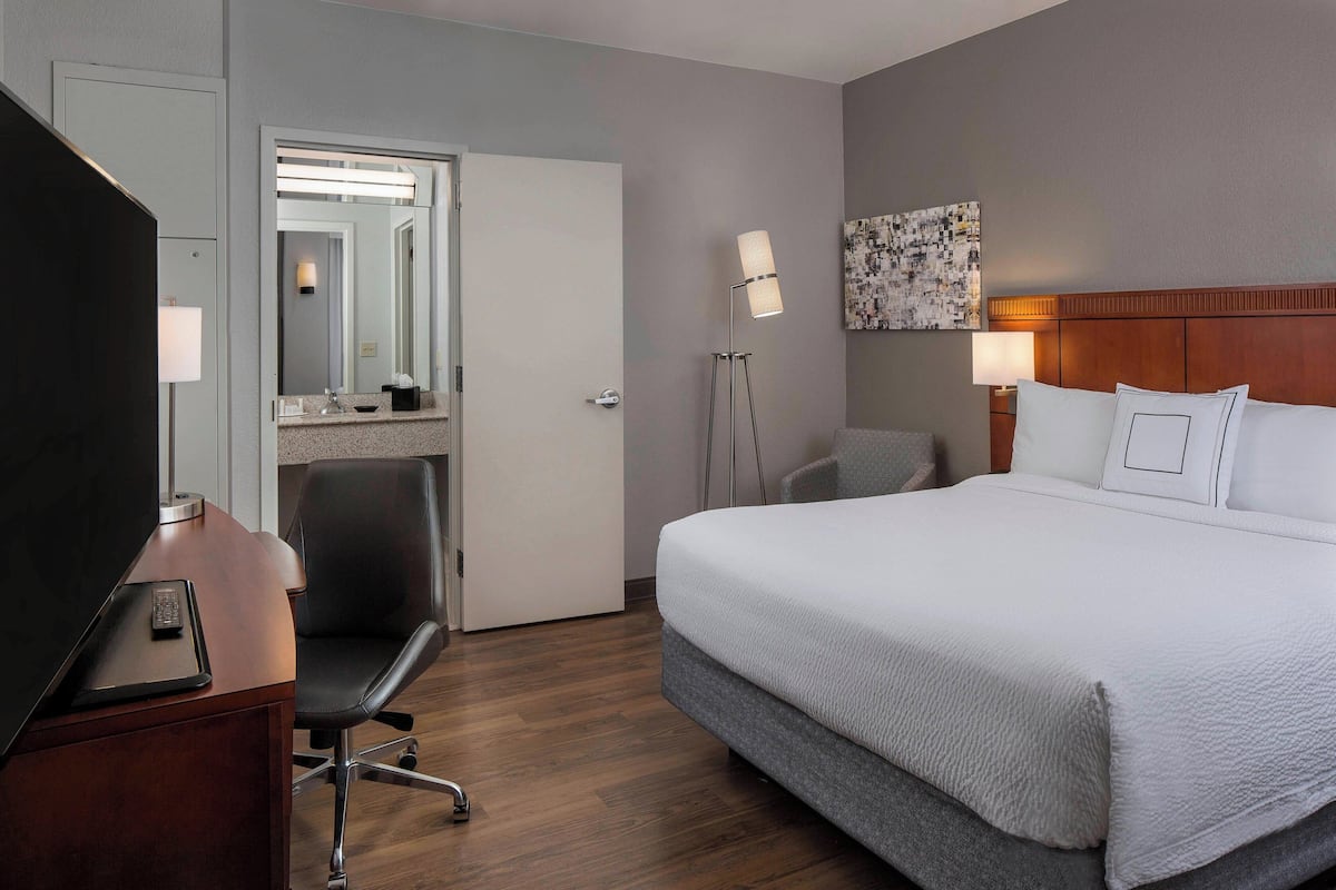 Hotellihuone, jossa on sänky, työpöytä, jossa on tietokone, tuoli, pöytävalaisin ja seinälle ripustettu taideteos.