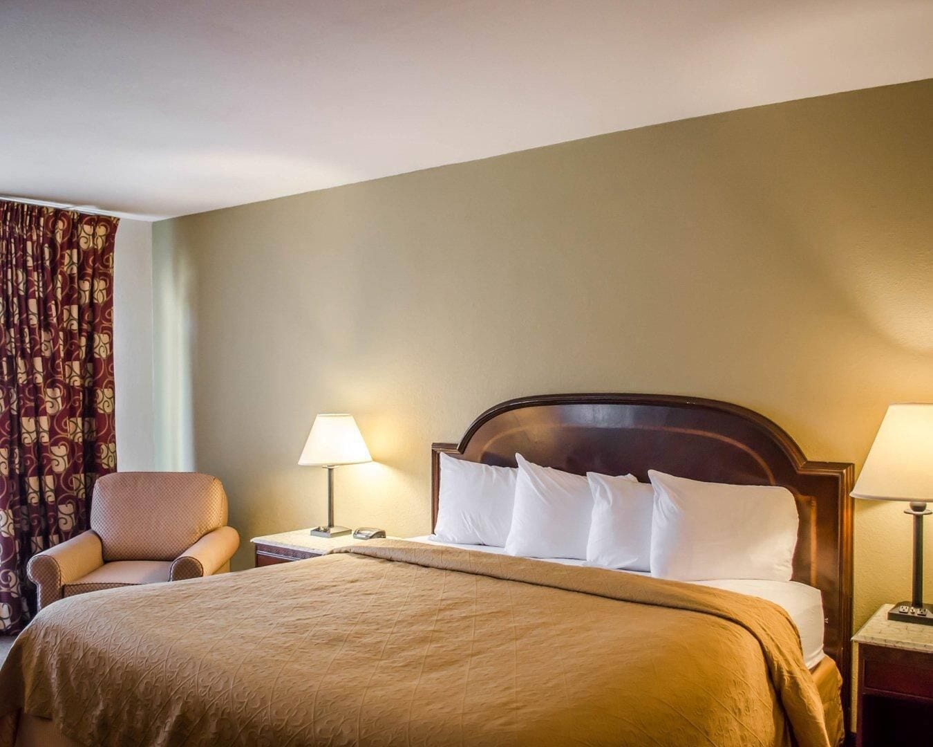 A hotel room with a bed, two bedside lamps, a chair, and a curtain.