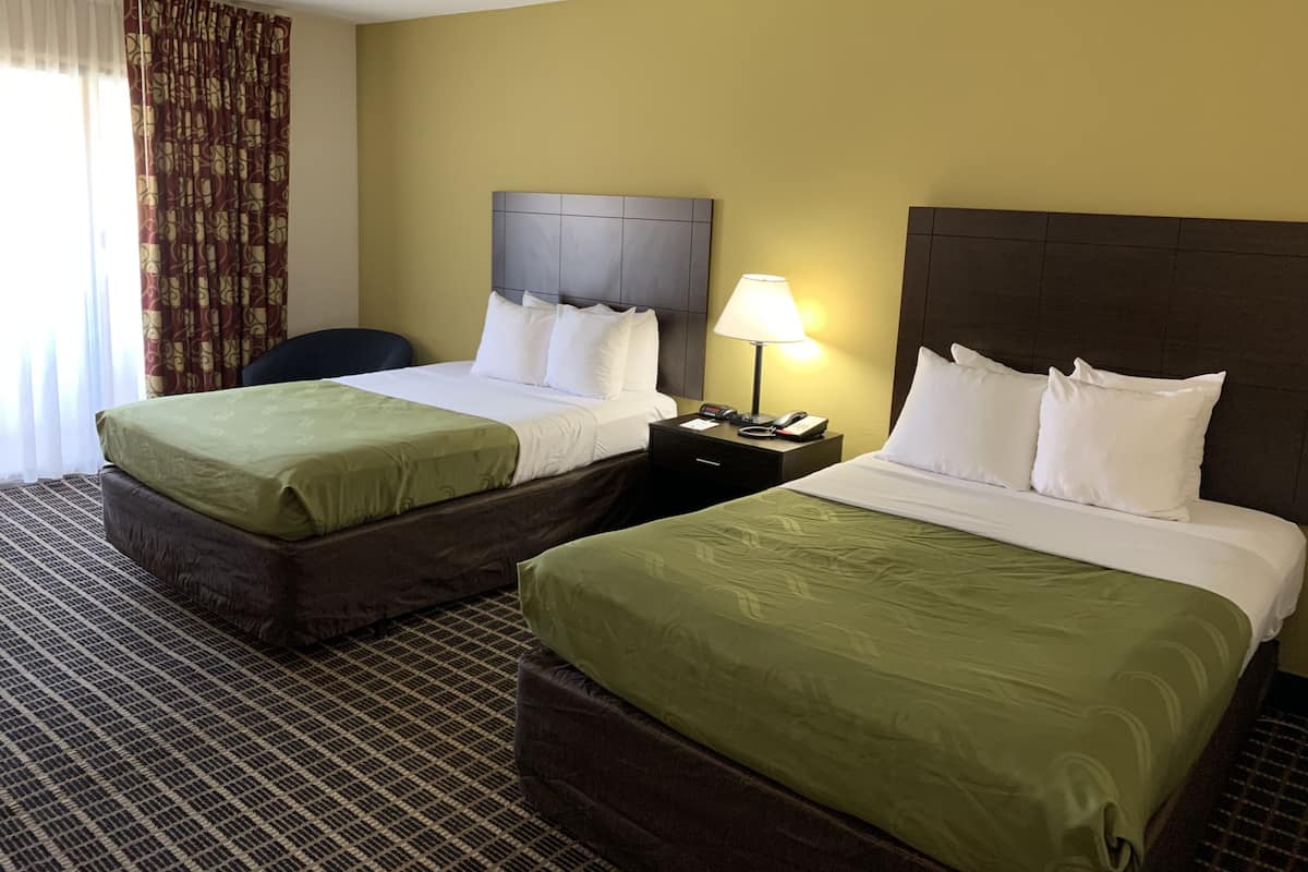 A hotel room with two beds, a nightstand with a lamp, and a check-in desk.