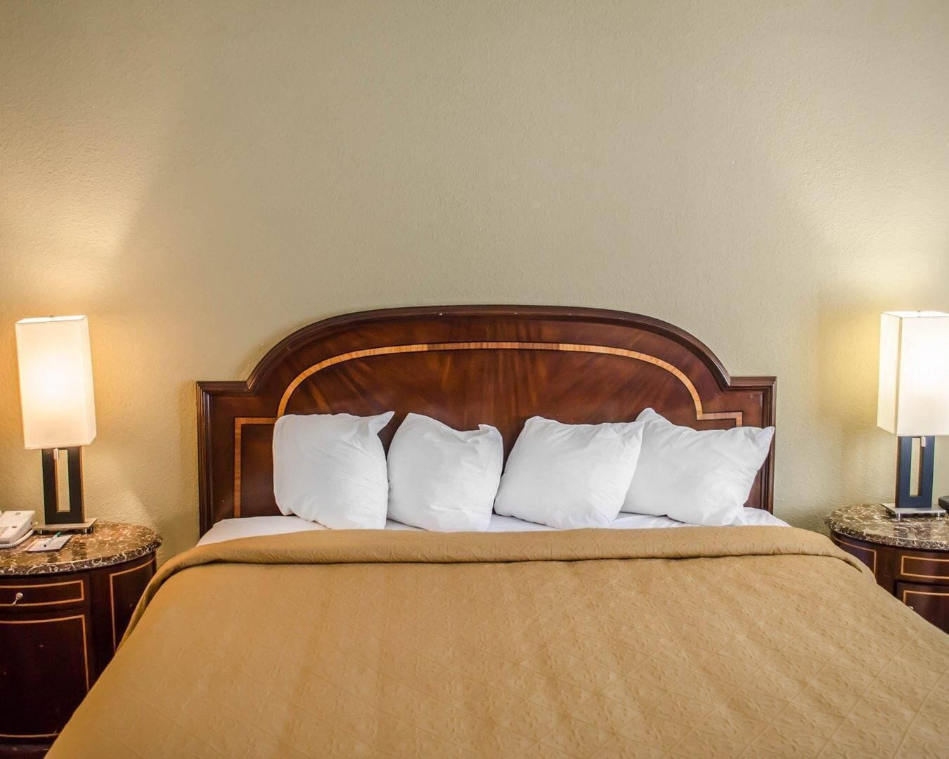 A hotel room with a wooden headboard, a bed with white bedding, and two bedside lamps.