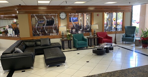 A hotel lobby with a black leather sofa, teal and red chairs, a coffee table, and a clock on the wall. - Quality Inn & Suites Pensacola Bayview (Pensacola)