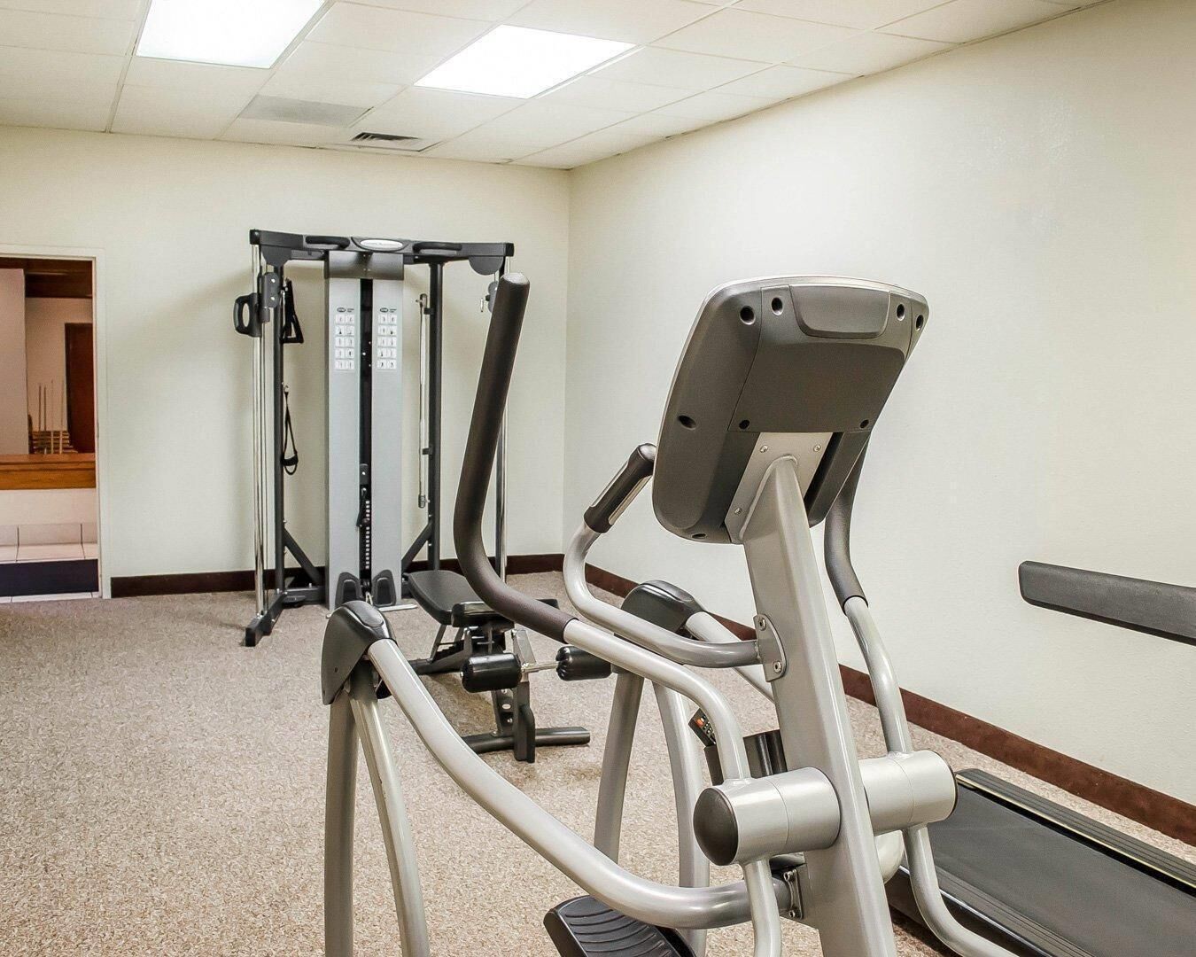 A gym with exercise equipment including a treadmill, elliptical, and weight machines.