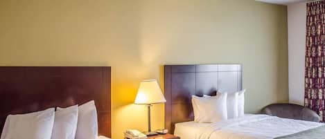 A hotel room with two beds, a nightstand with a lamp, a telephone, and a chair.