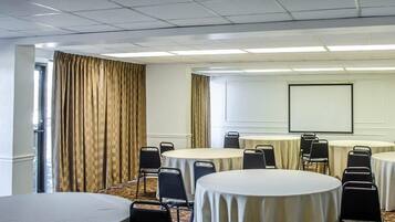 Une salle de conférence dotée de plusieurs tables rondes, de chaises noires, d’un écran de projection et d’une grande fenêtre avec des rideaux.