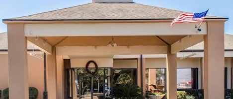 A hotel entrance with a covered waiting area, an American flag, and a wreath on the door.