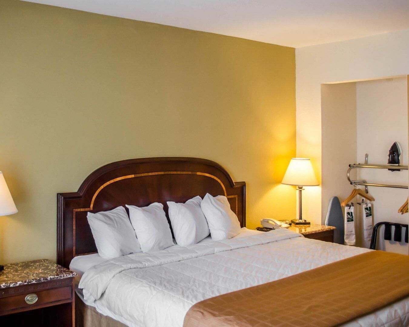 A hotel room with a large bed, two bedside tables, a lamp, a telephone, and a mirror.