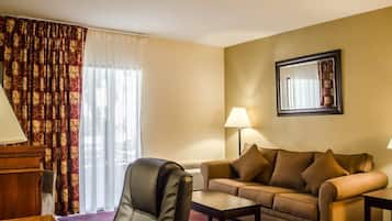 A hotel room with a leather chair, a sofa, a coffee table, a lamp, and a large window with curtains.