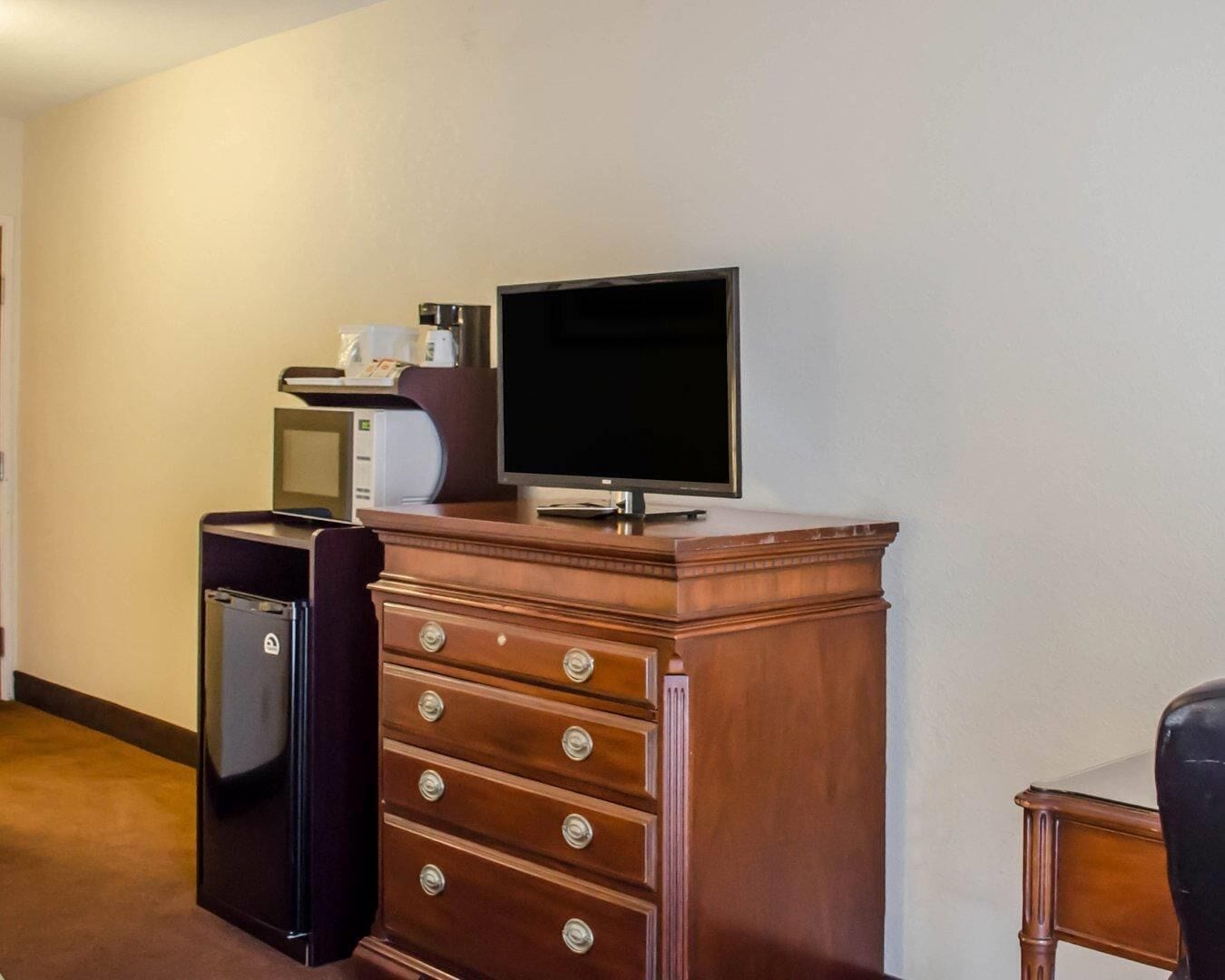 Habitación de hotel con cómoda de madera, televisor, refrigerador pequeño y escritorio con silla.