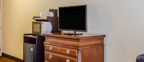 Habitación de hotel con cómoda de madera, televisor, refrigerador pequeño y escritorio con silla.