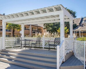 A covered outdoor area with a wooden deck, white lattice fence, and outdoor seating. - Quality Inn & Suites Pensacola Bayview (Pensacola)