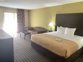 Une chambre d’hôtel avec un grand lit, un bureau, une chaise, une lampe et une fenêtre avec des rideaux.