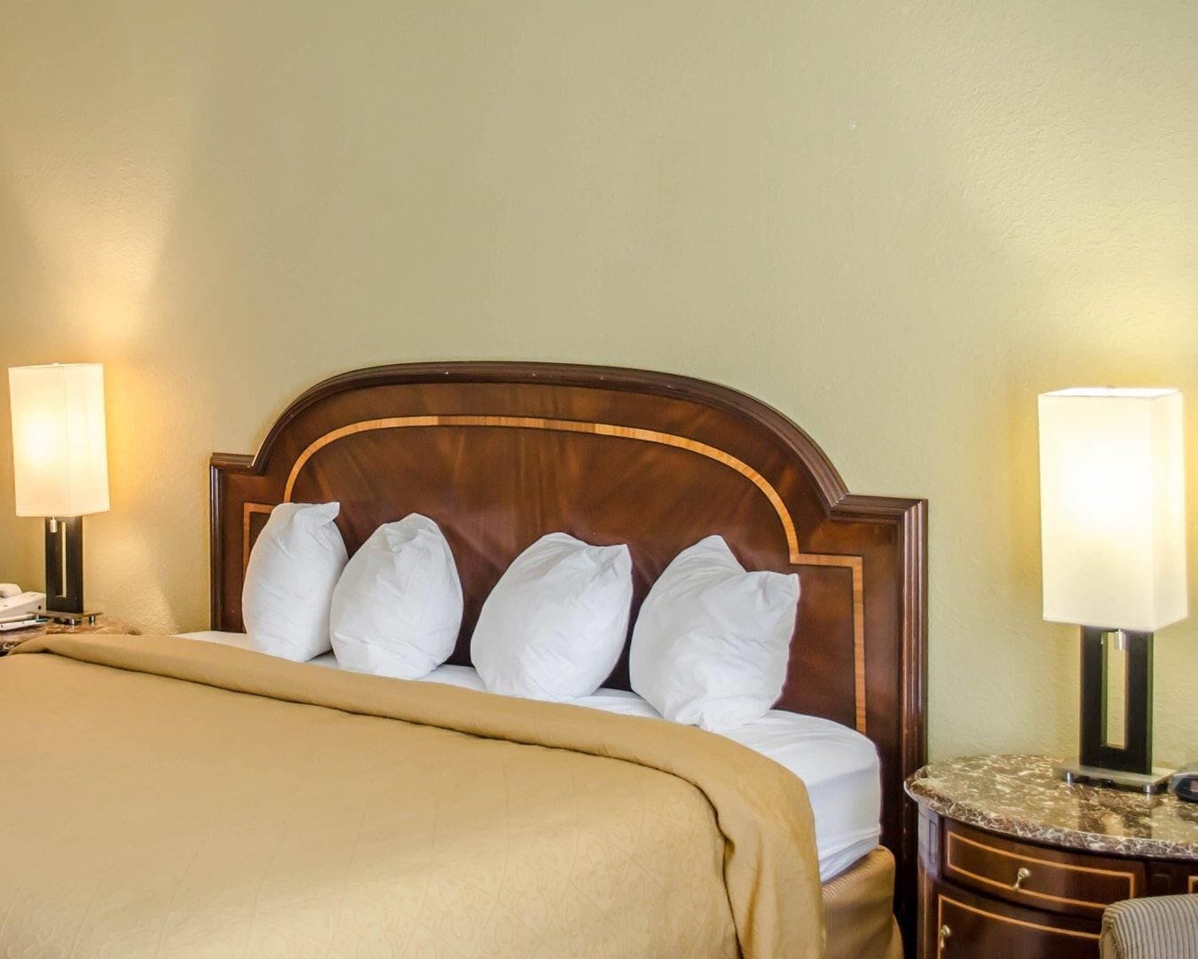 Quarto de hotel com uma cama, duas luminárias de cabeceira, um criado-mudo e uma mesa com tampo de mármore.