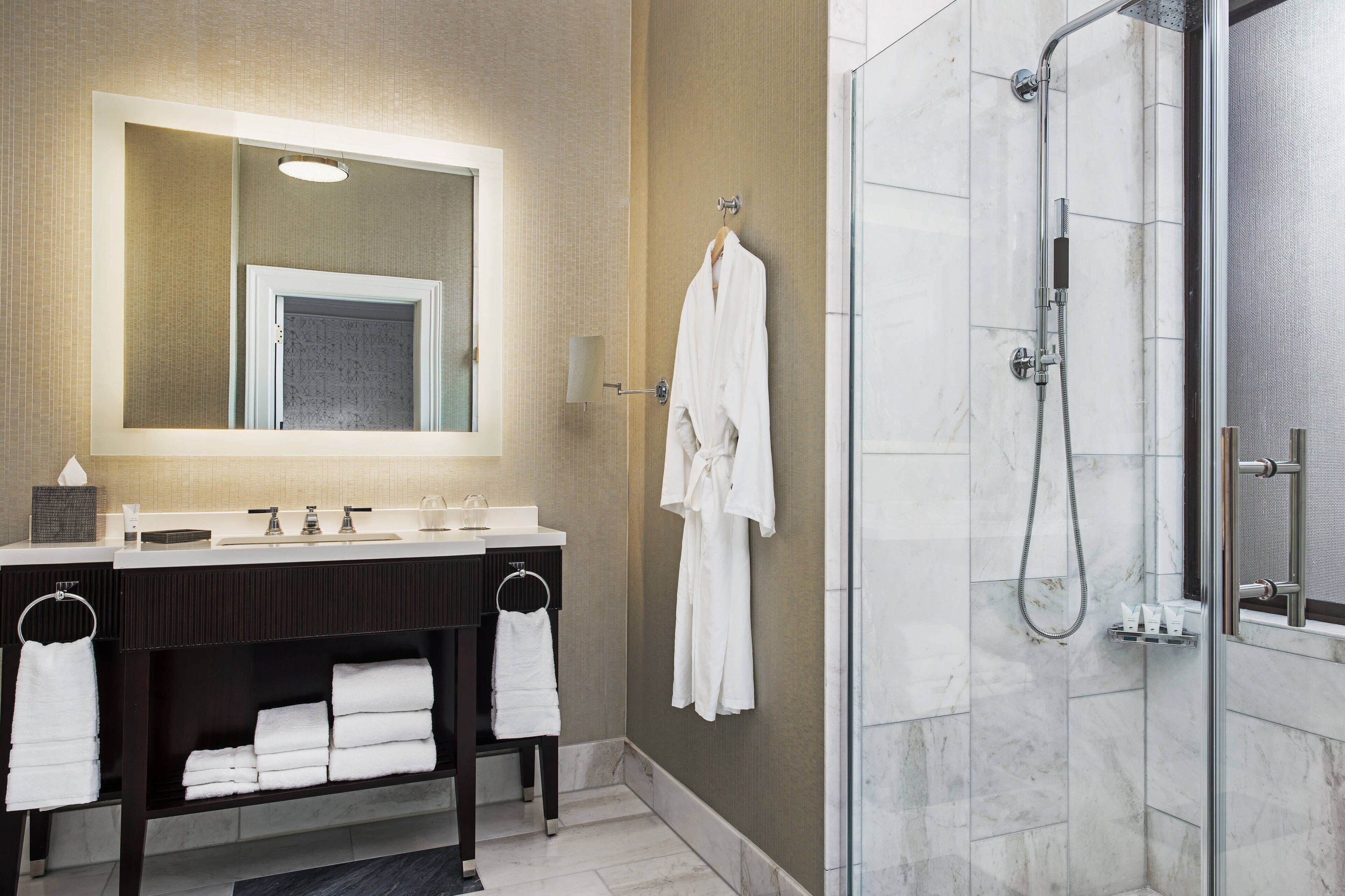 A modern bathroom with a large mirror, dual sinks, a glass shower enclosure, and neatly folded towels.