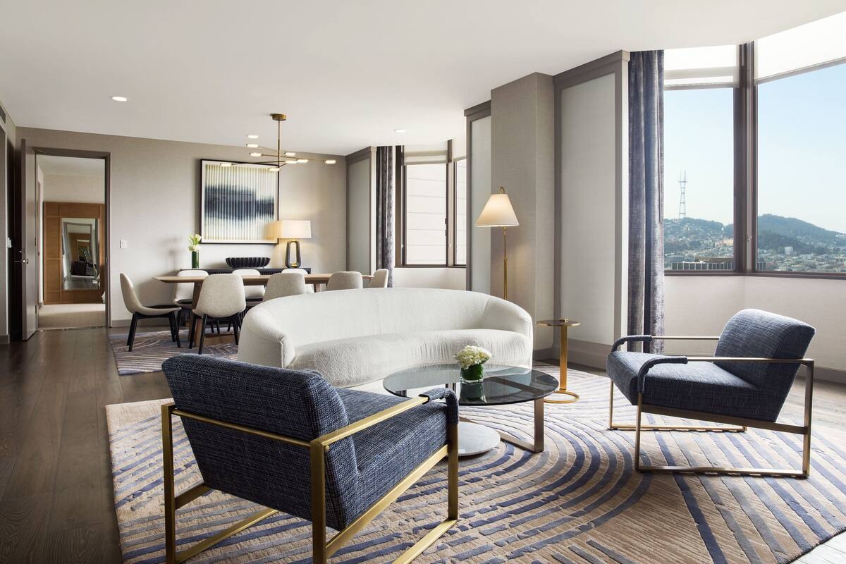 Een moderne hotelkamer met een groot bed, twee fauteuils, een salontafel en een eethoek.