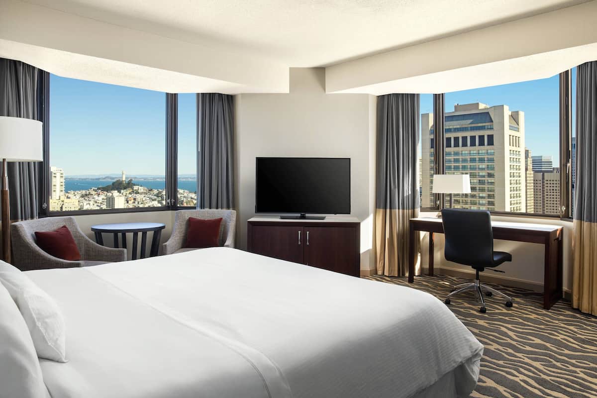 Een hotelkamer met een groot bed, een bureau, een televisie en uitzicht op een stadsbeeld.