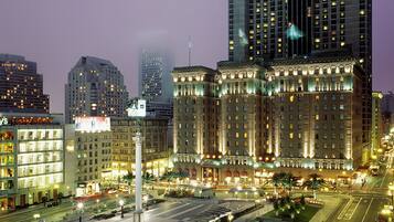 A cityscape at night with illuminated buildings, a prominent hotel with classical architecture, and a well-lit street.