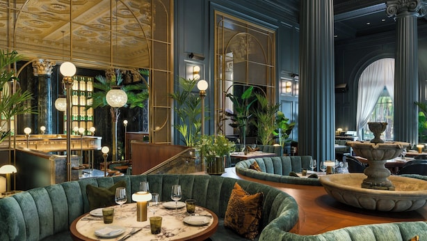 Un intérieur luxueux avec une table de salle à manger ronde, des sièges recouverts d’un tissu vert et une fontaine centrale.