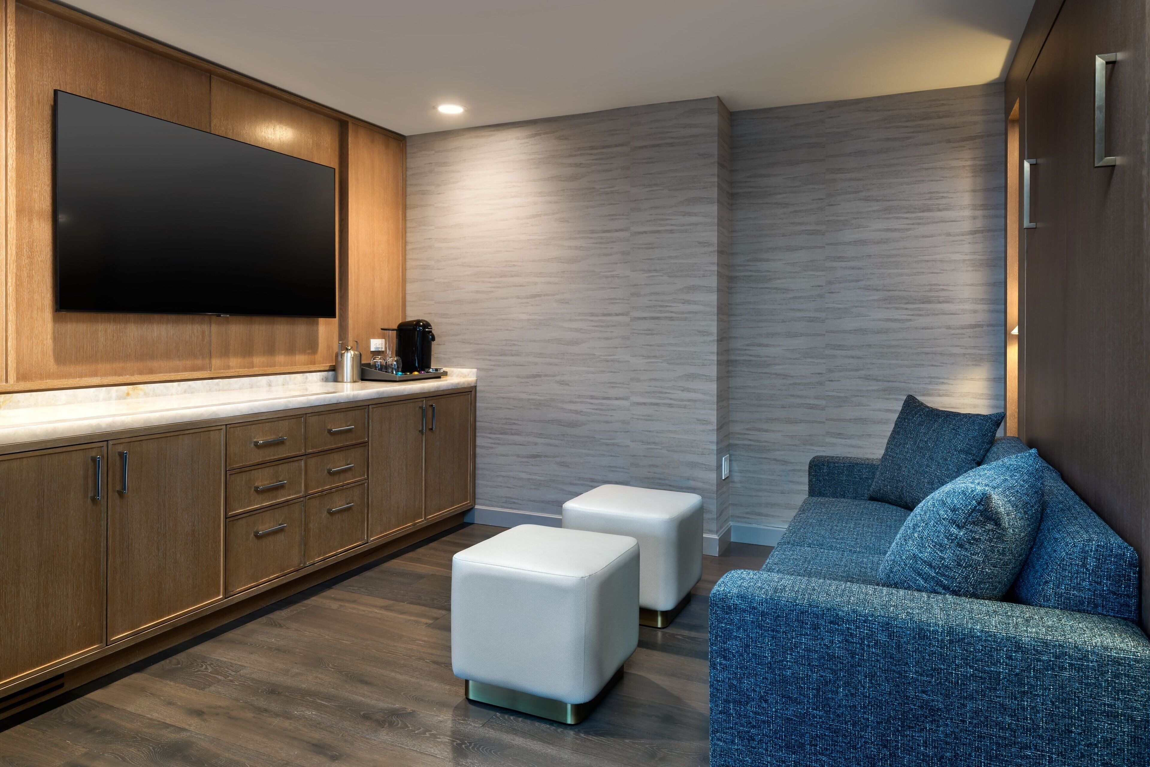 A modern kitchen with wooden cabinets, a large flat-screen TV, and a coffee maker.