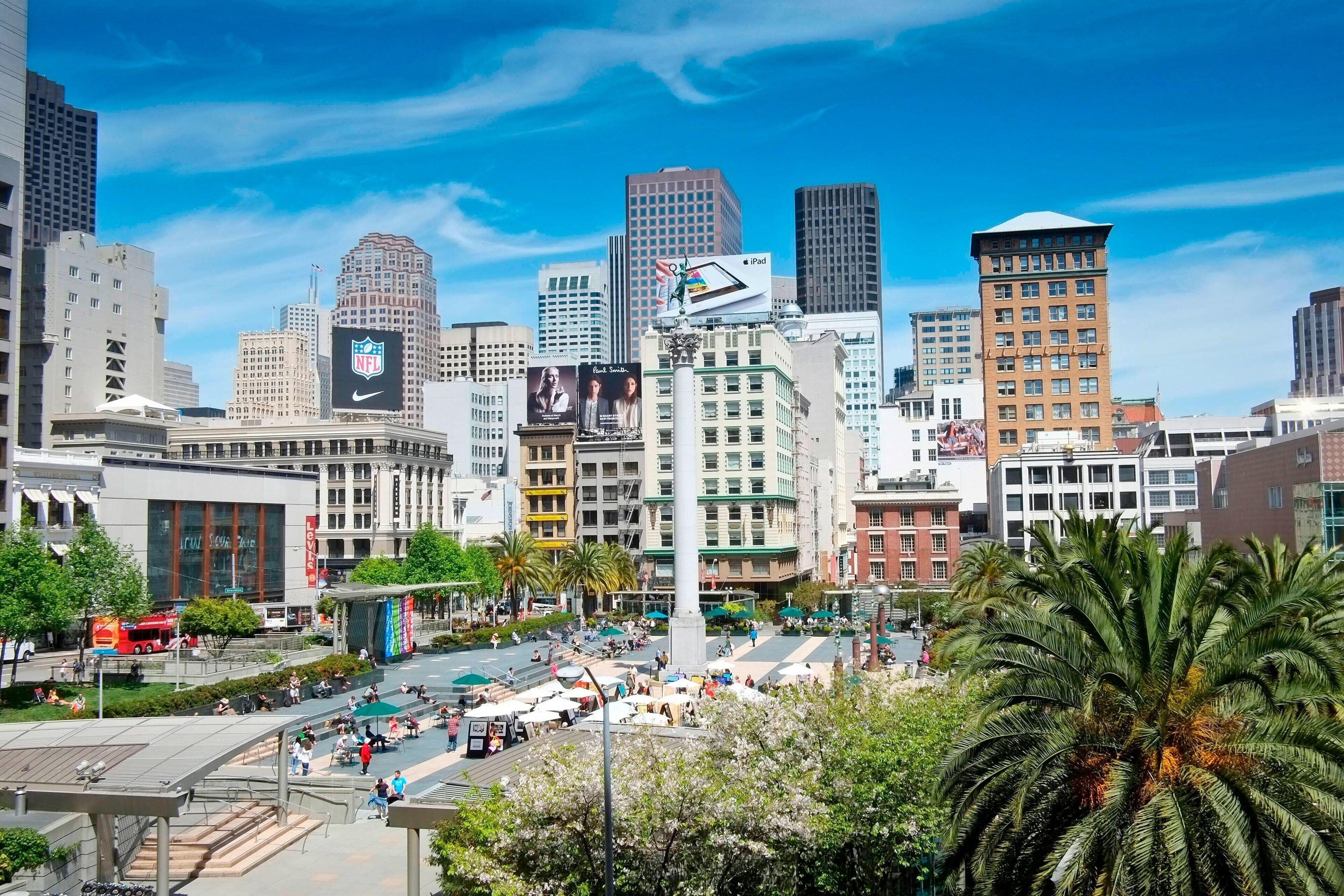 A cityscape with modern buildings, a prominent NFL sign, and a busy public square with palm trees.