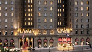 Un hôtel à plusieurs étages, doté d’une façade symétrique, de grandes fenêtres et d’une entrée centrale surmontée d’un auvent rouge.