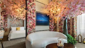 Une chambre d’hôtel avec un canapé blanc, une table ronde en bois et un grand téléviseur.