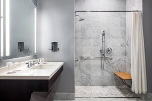 A modern bathroom with a large mirror, two sinks, a shower with a glass door, and a wooden bench.