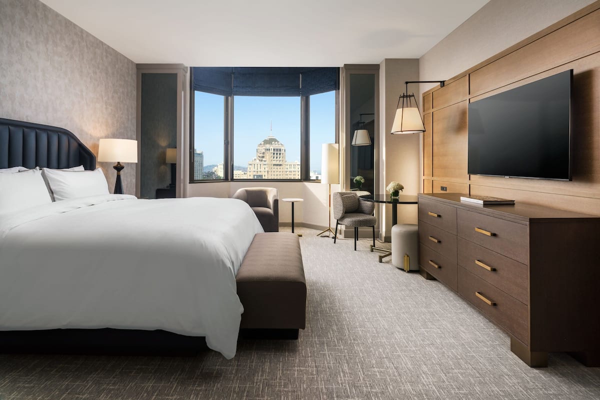 Een moderne hotelkamer met een groot bed, een flatscreen televisie, een bureau en uitzicht op een stadsbeeld.