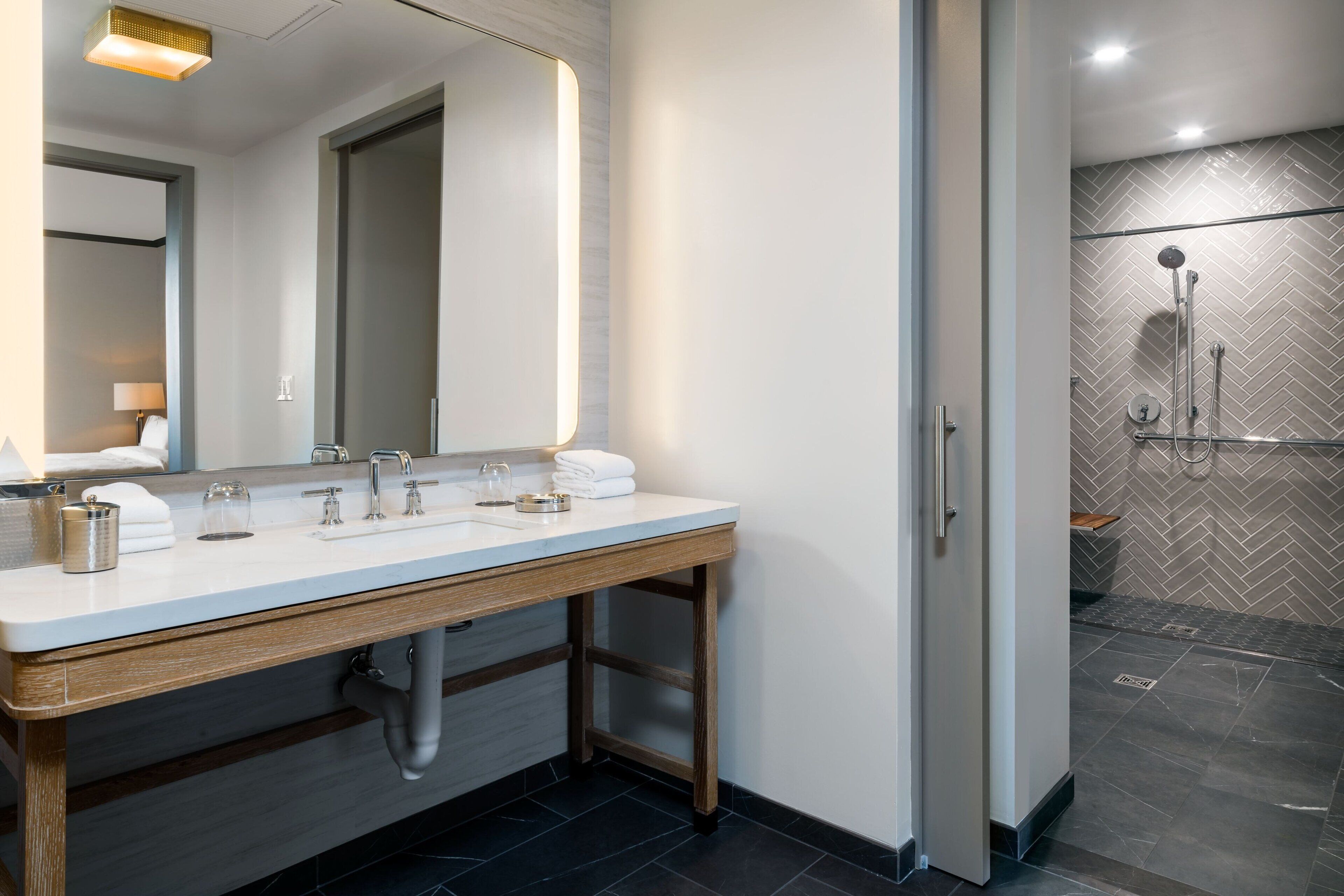A modern bathroom with a large mirror, two sinks, and a shower area.