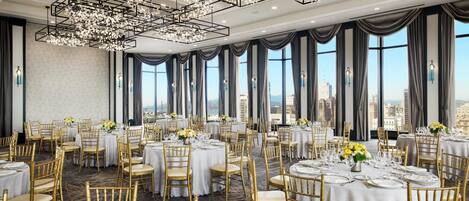 A banquet hall with round tables, gold chairs, and chandeliers.