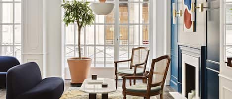 A modern living room with a large window, a potted plant, a coffee table, and two chairs.
