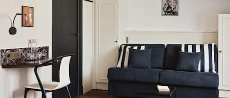 Una sala moderna con un sofá azul oscuro, una silla blanca, una pequeña mesa de centro negra y una encimera de mármol con una botella de agua y vasos.