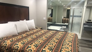Una habitación de hotel con una cama grande, baño independiente con ducha y un espejo.