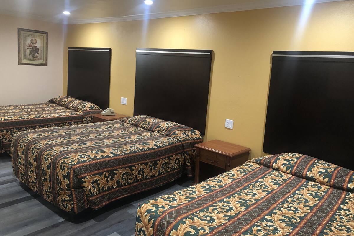 Une chambre d’hôtel avec trois lits, chacun recouvert d’une couvre-lit à motifs, une table de chevet avec un téléphone et un luminaire fixé au mur.