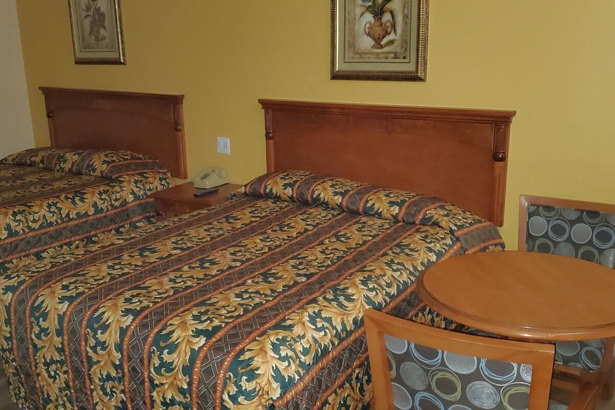 Une chambre d’hôtel avec deux lits, une tête de lit en bois, une table ronde et un fauteuil à motifs.
